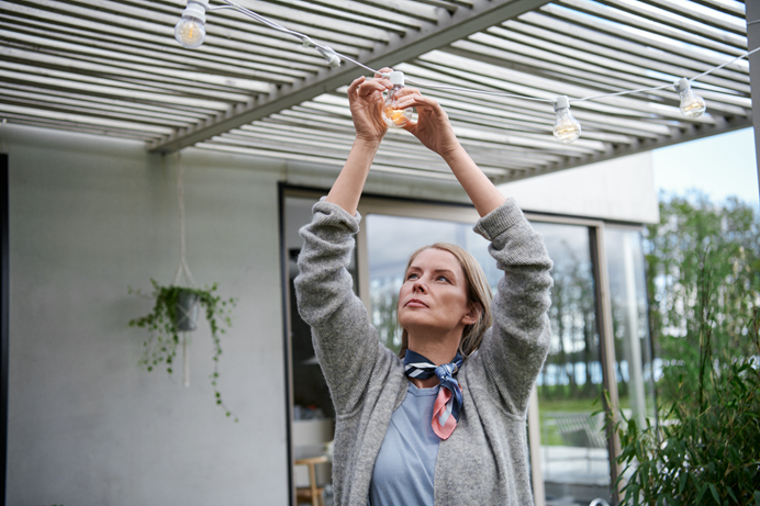 Vrouw hangt lampjes aan de pergola - buitenmuren isoleren