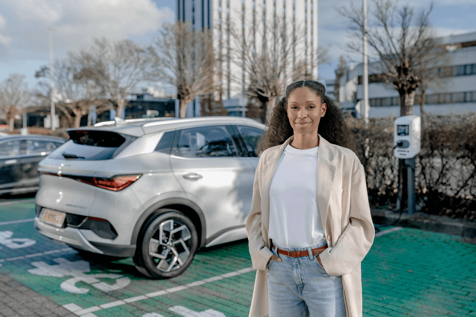 Vrouw staat voor een elektrische auto en zakelijke laadpaal