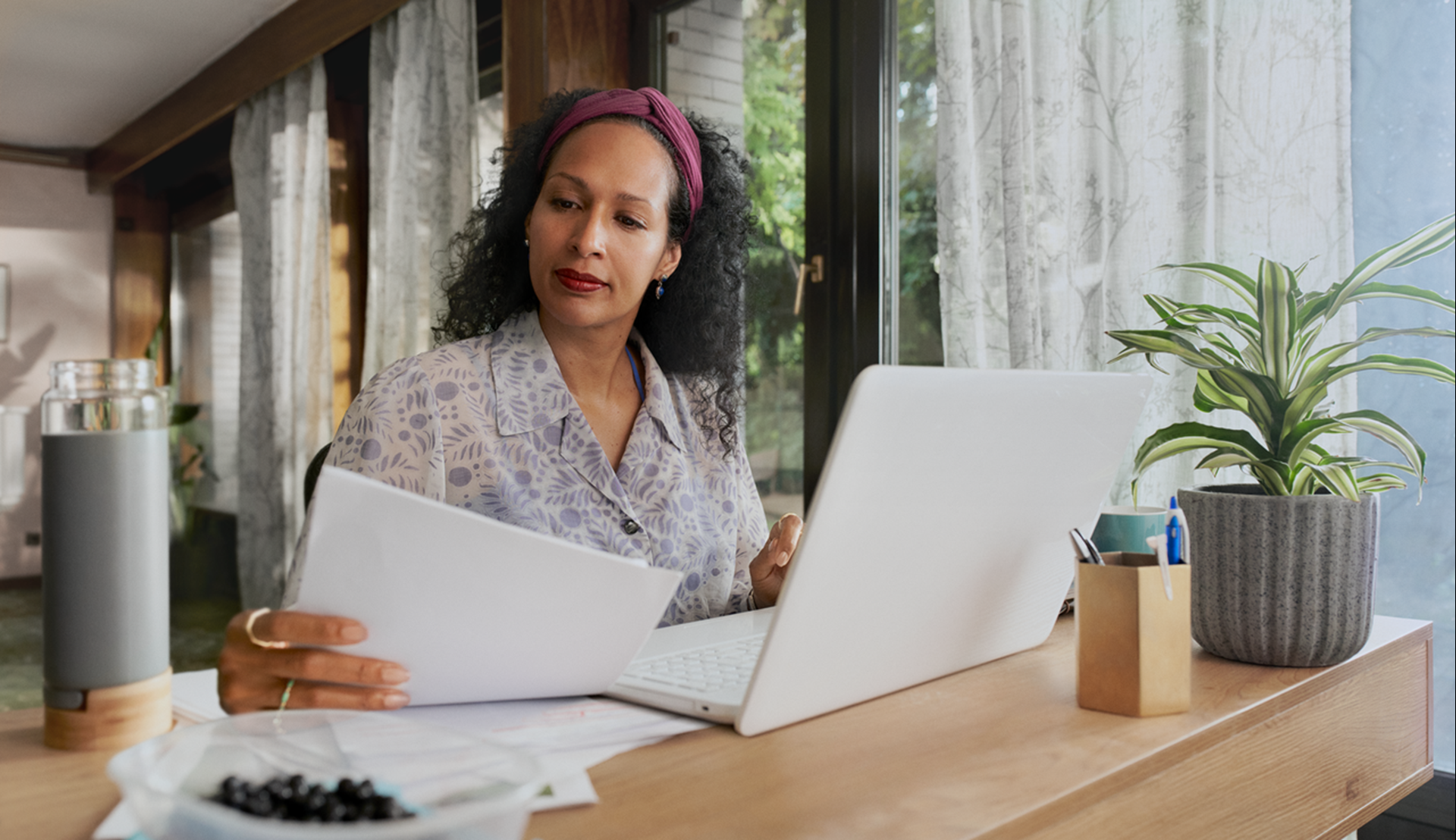 Vrouw kijkt naar papieren die naast haar laptop liggen