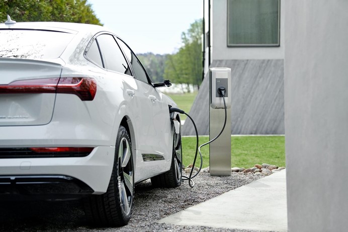 Vrouw laadt elektrische auto op aan laadpaal thuis