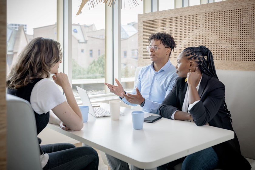 Twee vrouwen luisteren aandachtig naar een man achter een laptop 