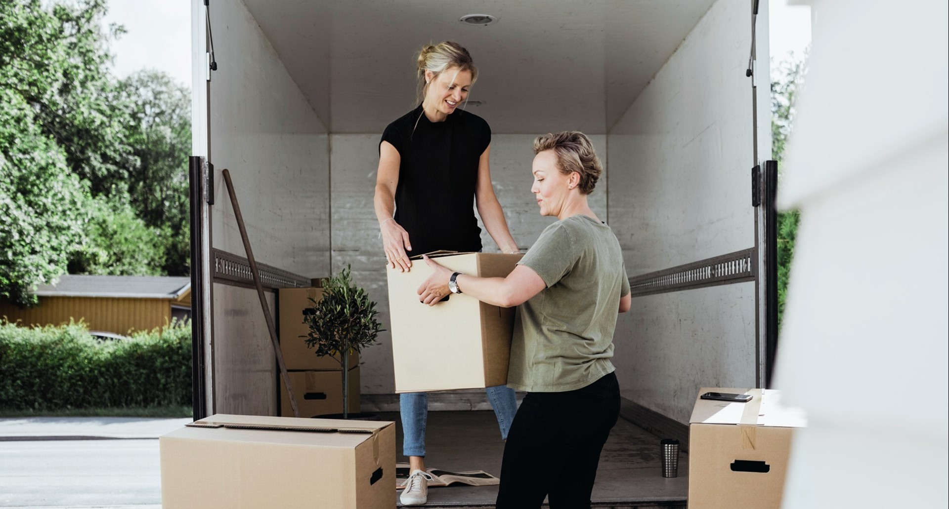 Twee vrouwen halen verhuisdozen uit een verhuiswagen