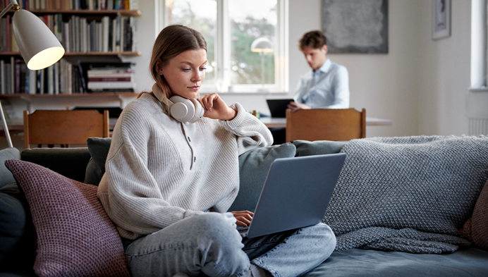 Jonge vrouw die met een laptop op schoot zit op een bank