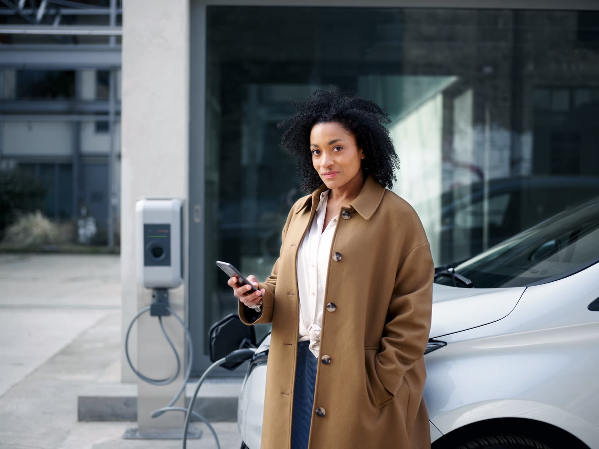 Een zzp'er leunt tegen haar auto terwijl ze die oplaadt