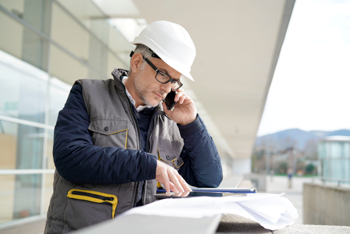 Man met helm belt met opdrachtgever over bouwproject