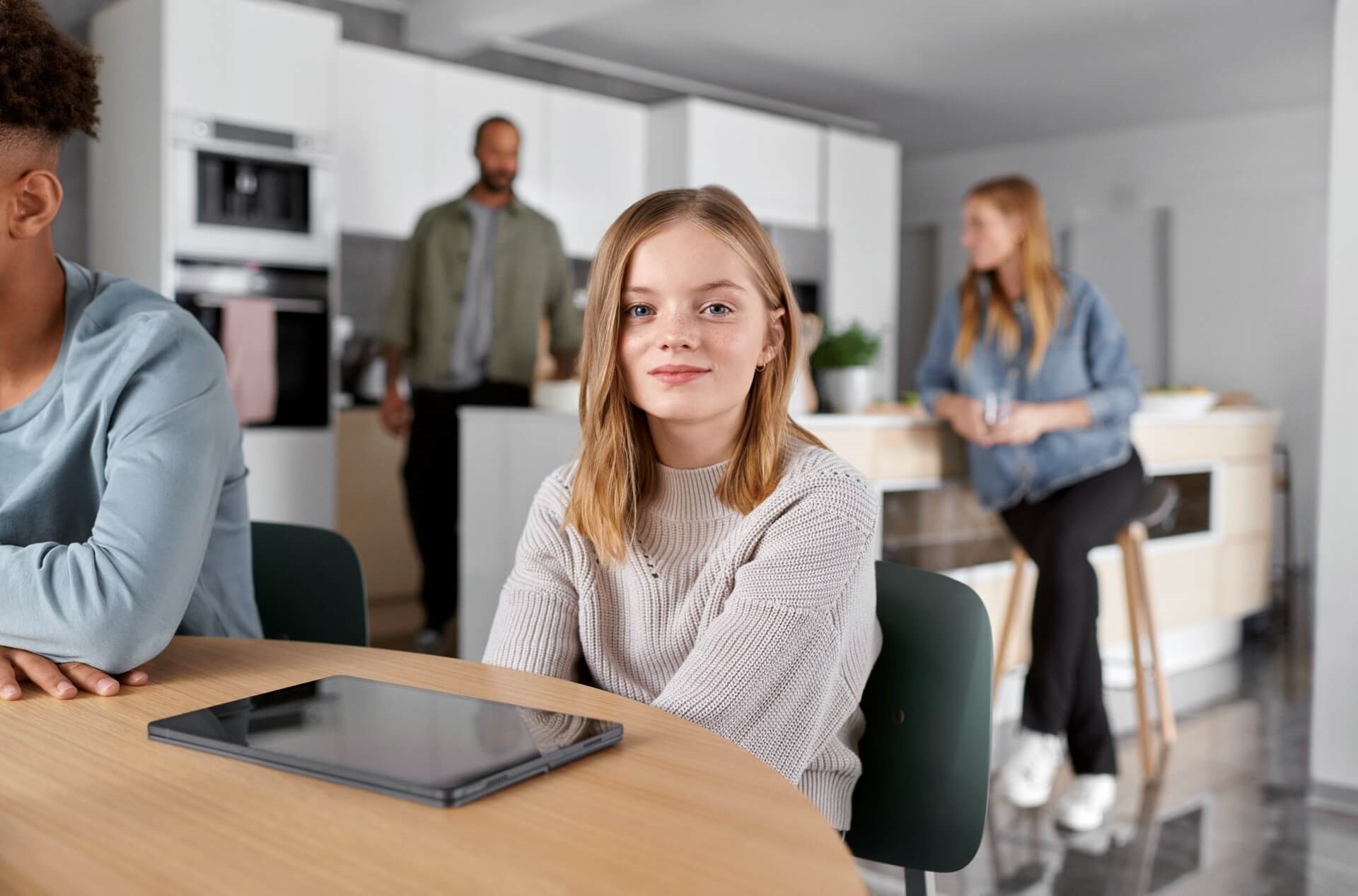 Vriendelijk meisje zit aan de keukentafel met familie en vrienden op de achtergrond | Vattenfall over gemiddeld energieverbruik