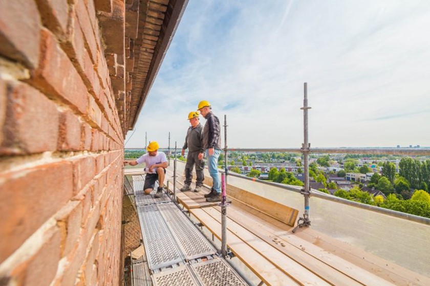 Werklui staan op een steiger bij een muur