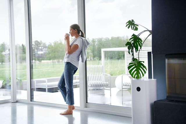 Vrouw staat met blote voeten op de vloer en kijkt uit het raam