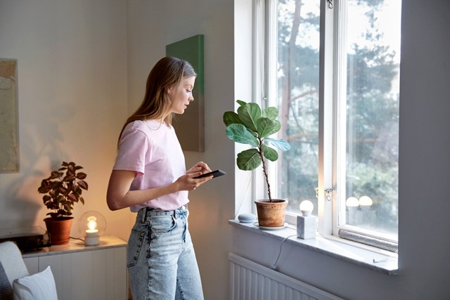 Jonge vrouw in roze shirt met mobiel in de hand kijkt uit het raam en denkt na over vast contract