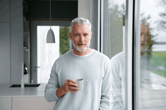 Grijze man bij het raam met kop koffie - Blijven Loont