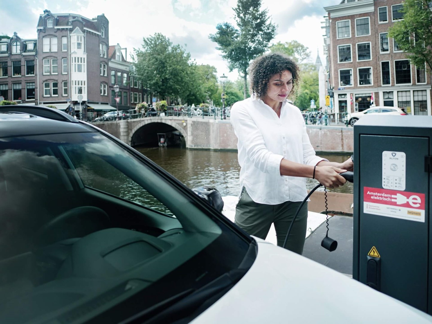 vrouw die elektrische auto aansluit op openbare laadpaal 