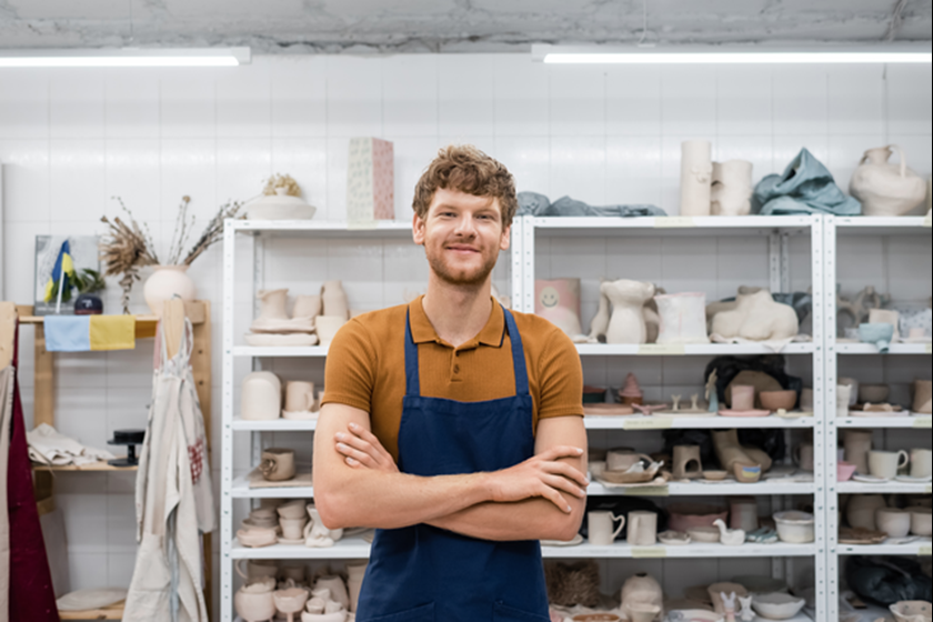 Een pottenbakker staat in zijn atelier en kijkt lachend de camera in