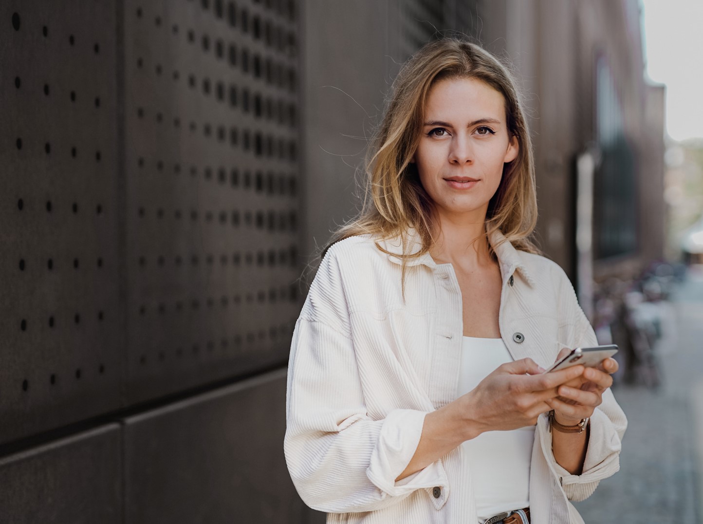 Vrouw staat met een mobiele telefoon in haar hand en kijkt in de camera